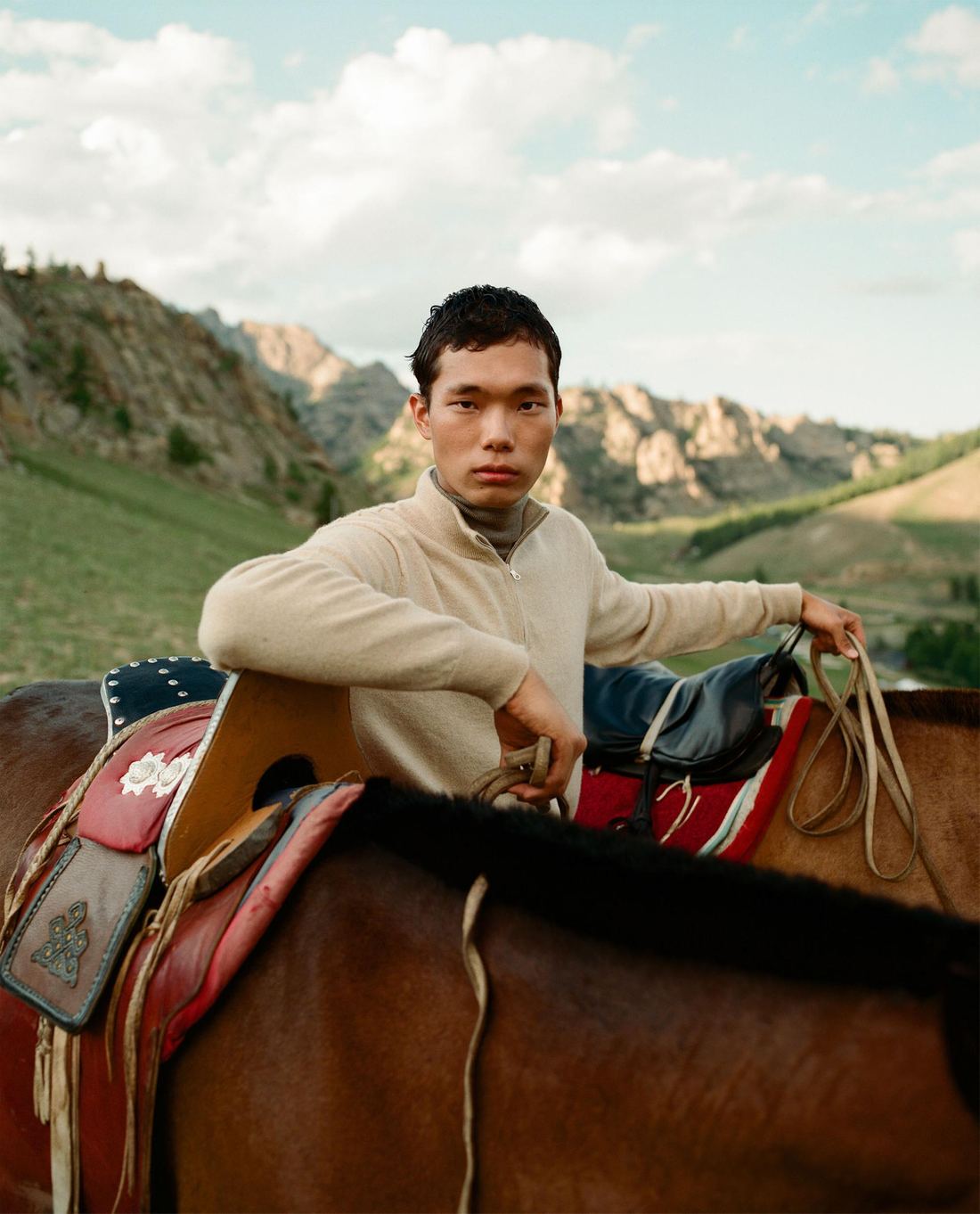 Young rider leaning on a saddled horse, looking into camera