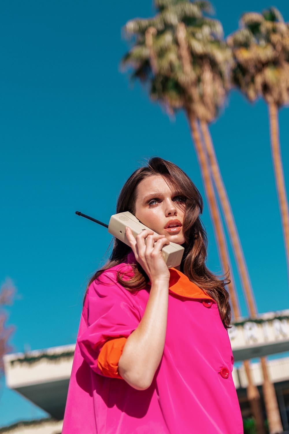 Woman in pink coat on a retro telephone under palm trees